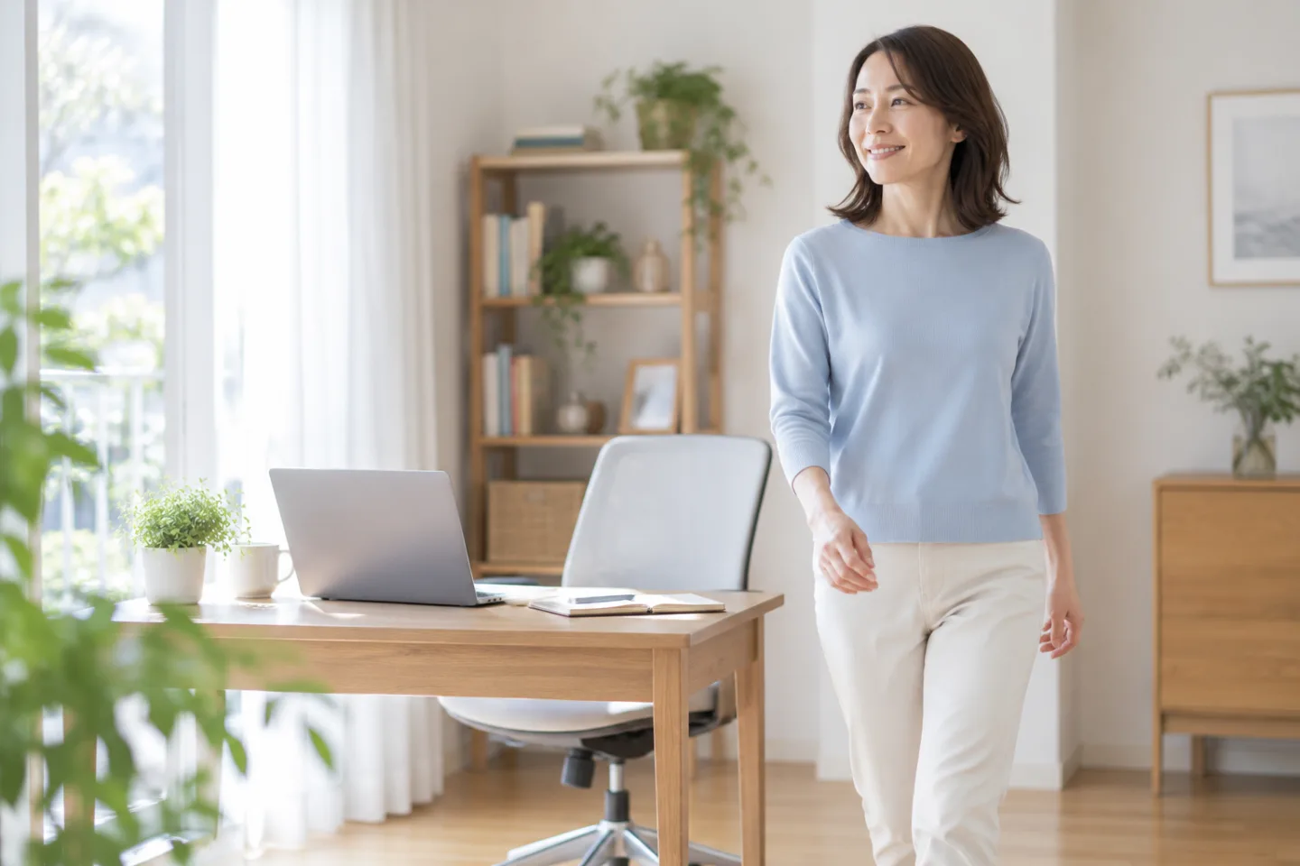 明るい自宅の仕事机を離れて歩く40代女性のイメージ