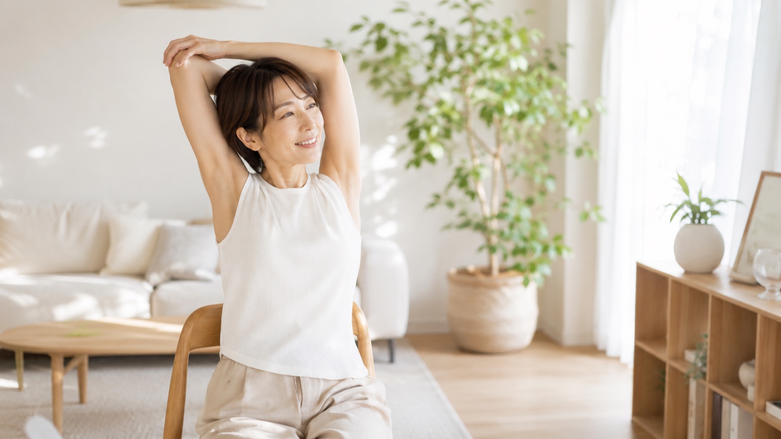 椅子に座ったまま二の腕を引き締めるエクササイズをする40代女性のイメージ